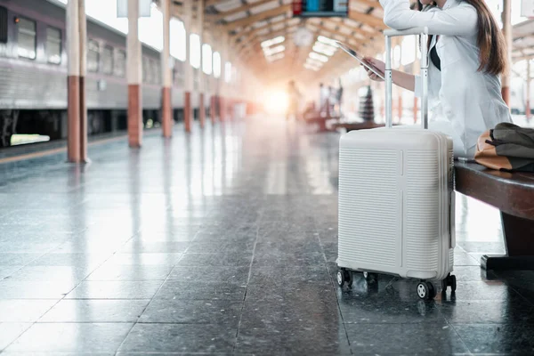 Bavul ve tabletli bir gezgin güneşli bir tren istasyonunda bekliyor, seyahat ve beklentinin özünü yakalıyor..