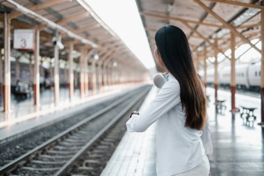 Kulaklıklı bir kadın tren istasyonunda modern seyahatleri ve seyahatleri sembolize ediyor..