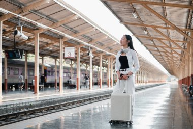 Tren istasyonunda bavullu bir kadın, güneşli bir çatı altında uzaklığa bakıyor..