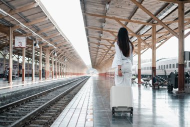 Tren peronunda elinde bavuluyla gezmeye hazır bir kadın var. İstasyon boş, bir beklenti hissi yaratıyor..