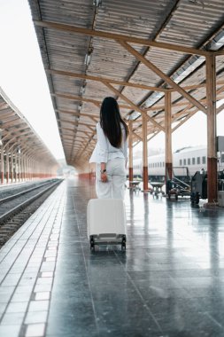 Tren istasyonunda bavullu beyaz elbiseli bir kadın, seyahat ve macera sergiliyor..
