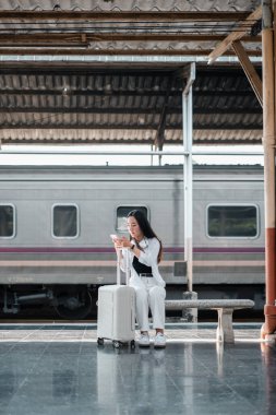 Tren istasyonunda bavullu bir kadın oturuyor, harita okuyor. Seyahat ve keşif konsepti.