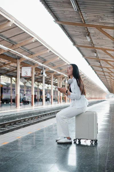 Tren istasyonunda bavulda oturan, kulaklık takan, seyahat etmeye hazır bir kadın..