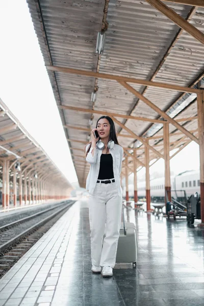 Tren istasyonunda bavullu bir kadın, telefonla konuşuyor, seyahat macerasına hazır. Gündelik tarz, modern yolculuk..