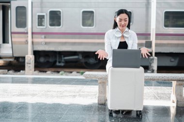 Tren istasyonunda dizüstü bilgisayar kullanan, kulaklık takan, arka planda tren kullanan bir kadın..