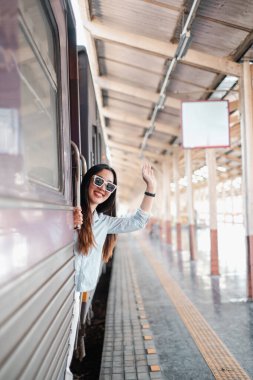 İstasyondaki tren penceresinden el sallayan neşeli kadın seyahat ve maceranın neşesini yakalıyor..