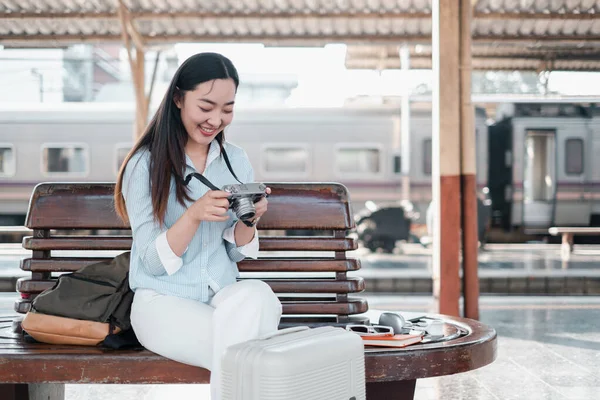 Tren istasyonunda bankta oturan gülümseyen kadın, kameradaki fotoğrafları inceliyor. Seyahat ve macera konsepti.
