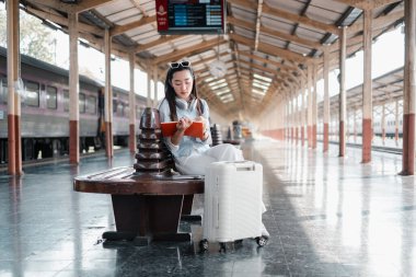 Tren istasyonunda bavulla kitap okuyan bir kadın. Seyahat, keşif ve modern macera..