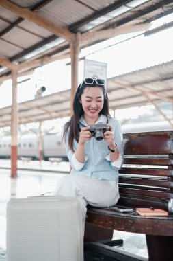 Tren istasyonunda kamera ve bavulla gülümseyen kadın, seyahat macerasına hazır..