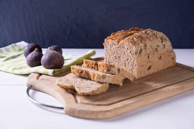 Beyaz bir masada, üzerinde taze dilimlenmiş ekmek ve mavi bir zemin üzerinde olgun incirler olan bir tahta.