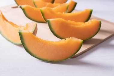 Ön planda olgun bir kavun dilimi, tahta tahtası ve beyaz arka plan.