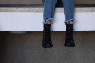 Bacaklar, siyah botlar içinde, korkuluklardan aşağı itilmiş, sallanıyor.