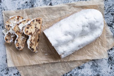 Dilimlenmiş noel pastası badem ezmesi, fındık ve kuru üzümler parşömen kağıdının üstünde.
