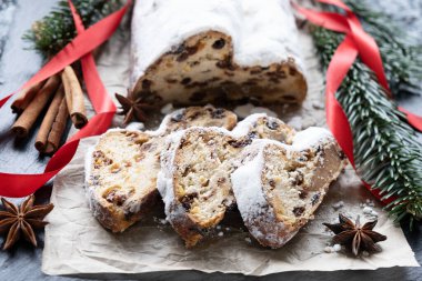 Badem ezmeli noel pastası, parşömen kağıdında fındık ve kuru üzüm, tarçın ve anason, desenli arka planda kırmızı kurdeleli ladin dalları