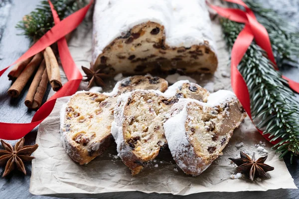 Badem ezmeli noel pastası, parşömen kağıdında fındık ve kuru üzüm, tarçın ve anason, desenli arka planda kırmızı kurdeleli ladin dalları