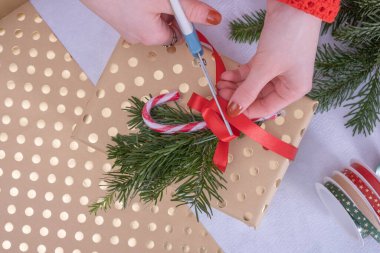 Kız ladin dalları ve kırmızı kurdeleyle Noel şekeri bağlayıp Noel hediyelerini süslüyor.