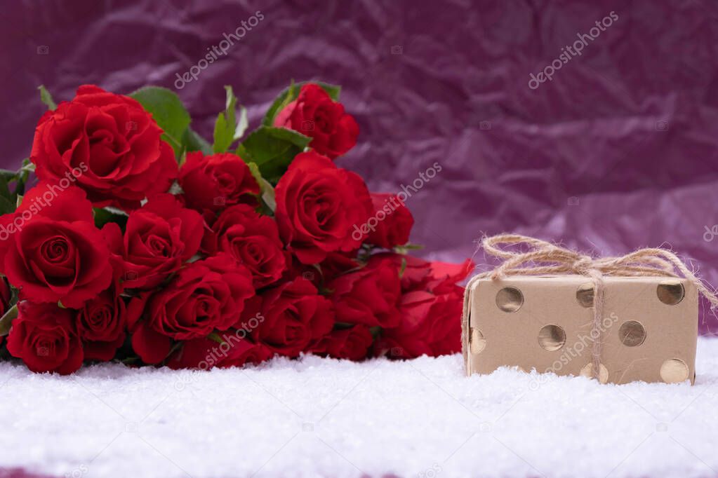 a bouquet of red roses lies in the snow on a pink background