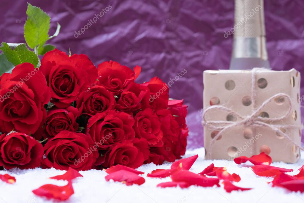 gift, a bouquet of red roses on white snow and a bottle of champagne on a pink background
