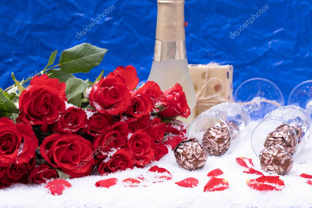 bouquet of red roses on a blue background, candies in the snow, next to a bottle of champagne, festive table