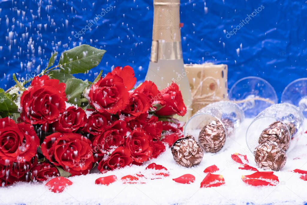 candies in the snow, a bouquet of red roses on a blue background, next to a bottle of champagne, a festive table