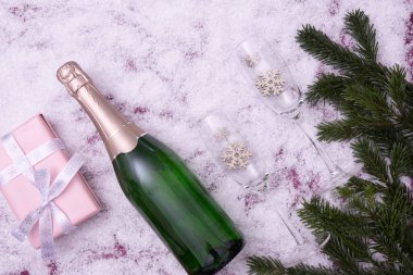 Şekerler, ladin dalları, bir hediye, şampanya ve şarap kadehleri karlı arkaplanda yazan 