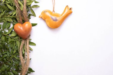 Taştan yapılmış bir kalp ve yeşil yaprakların yanındaki masada yatan demir bir kuş, beyaz bir arka planda, üst görünümde.