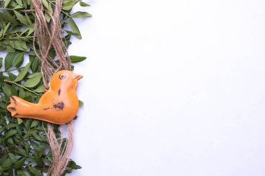 İpte metalden yapılmış kuş, yeşil yaprakların yanında, beyaz arka planda, üst görünümde.