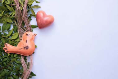 Metalden yapılmış bir kuş, taştan ve yeşil yapraklardan yapılmış bir kalbe yakın, beyaz arka planda, üst görünümde.