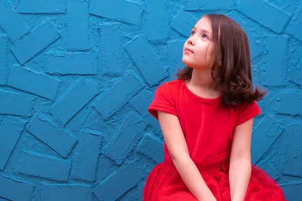 girl in a red dress sits on the floor and looks up and dreams, on a blue background