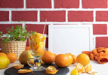 Portakal dilimleriyle dolu bir şarap bardağı ve bir fotoğraf çerçevesinin arkasında bir masa dolusu meyve.