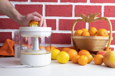 Meyve sıkacağı üzerine portakal suyu sık, masada bir sürü portakal ve meyve var, arkasında tuğla bir duvar var.