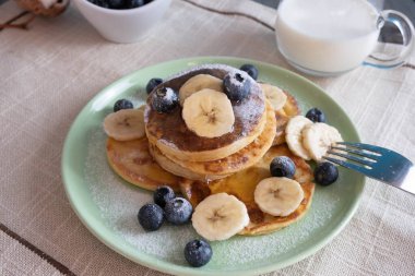 Taze pişmiş, böğürtlenli ve muzlu krep tabakta, yanında da masada süt var.