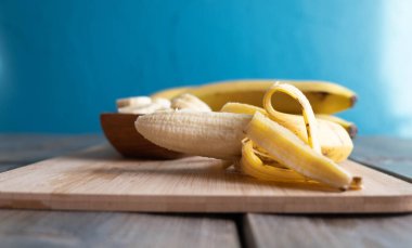 Ahşap bir tahtanın üzerinde açık bir muz yatıyor. Kesilmiş muzların arkasından. Tahta bir fincanda, bir masada yatıyor.
