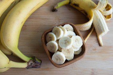 Muzlar ahşap bir tahtanın üzerinde yatar ve parçalara ayrılır. Muzlar masanın üzerinde, tahta bir fincanda yatar.