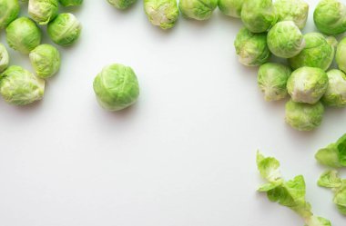 Olgun Brüksel lahanaları masaya yayılmış, yaprakları yanında, beyaz bir arka planda.