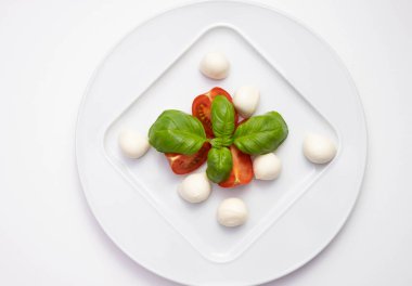 mozzarella, yeşil fesleğen ve domatesler beyaz tabakta ve beyaz tabakta.