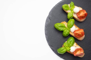 Üzerinde beyaz ekmek, mozzarella, taze fesleğen ve beyaz bir tabakta doğranmış domates var.