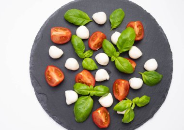 Bir taş tezgahında mozzarella, taze fesleğen ve beyaz arka planda doğranmış domates.