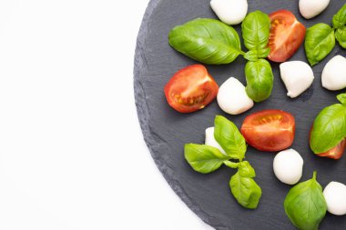 mozzarella, taze fesleğen ve domatesler beyaz arka planda siyah bir taş standı üzerine serilmiştir.
