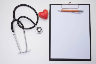 Stetoskop, masanın beyaz zeminindeki notlar için kırmızı kalp kağıdı.