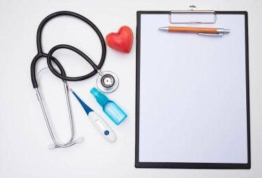 Stetoskop, kırmızı kalp, notlar için bir kağıt parçası, bir termometre ve masanın üzerinde beyaz bir arka plan üzerinde bir antiseptik.