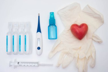 Lateks eldivenler, termometre, iğneler için su, taştan yapılmış kırmızı kalp, vitaminler, beyaz arka planda bir şırınga.