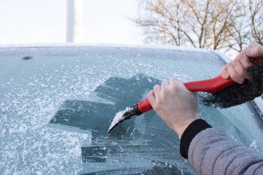 Erkek eli dışarıda, caddedeki buzdan arabanın camını temizliyor.