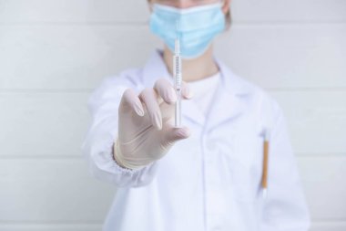 Doktor elinde bir ilaç olan bir şırınga tutuyor ve iğneyi beyaz arka planda yukarı çekiyor.