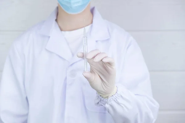 a doctor in a mask holds a syringe with a medicine in his hand upwards, on a white background