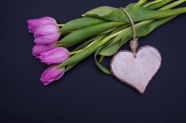 Sağ üstten, tahta bir kalp ve siyah arka planda küçük bir buket pembe lale.