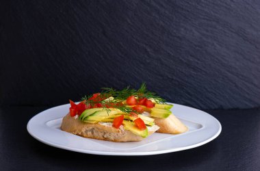 Avokado dilimlerinden kanepeler ve beyaz tabakta dereotu ve siyah arka planda bir dilim domates.