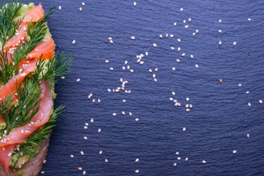 Avokado ve füme somon filetosu ile nefis kanepeler ve taze dereotları ve üzerine susam tohumları serpiştirilmiş siyah arka plan ve üst manzara, yakın çekim