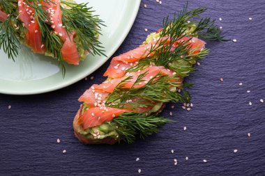 Avokado ve tütsülenmiş somon filetosu ve siyah arka planda taze dereotu filizi dilimleri.