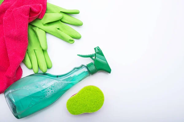 green gloves, window cleaning liquid and a pink rag lie on a white background
